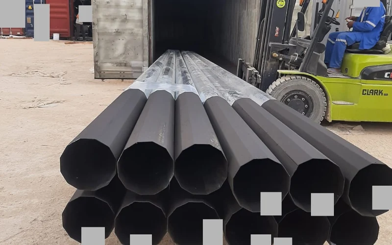 Manutention d’un faisceau de supports de ligne métalliques devant le conteneur